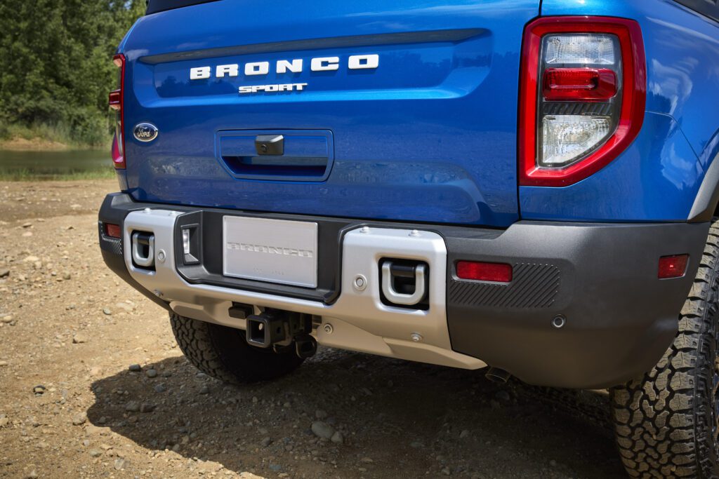 Rear side view of the 2025 Ford Bronco Sport Badlands in Velocity Blue parked by a river, highlighting its off-road design, black roof, and bold tailgate branding